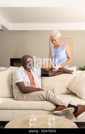 Diverse senior couple checking blood pressure on couch in living room, with digital monitor Stock Photo
