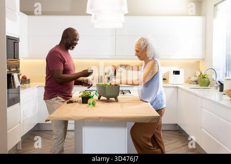 Preparing Diverse senior couple chopping veggies for salad at kitchen island, featuring green bowl Stock Photo