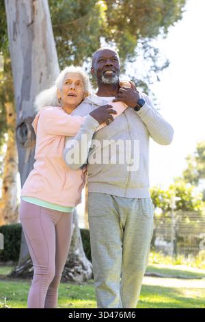 Hugging Diverse couple standing in grassy park under eucalyptus tree, with smartwatch on wrist Stock Photo