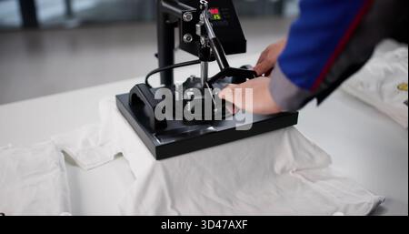 Man Designs Custom T-Shirt On Heat Press Printing Workshop Stock Photo