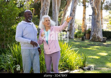 Talking diverse friends pointing toward right at sunny grassy park, with eucalyptus trees Stock Photo
