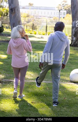 Mature White woman and senior African American man stretching leg in park with eucalyptus trees Stock Photo