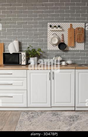 Interior of modern kitchen with white counters and pegboard hanging on grey brick wall Stock Photo