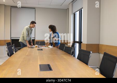 Collaborating diverse colleagues leaning on table in office, with tablet, laptop and documents Stock Photo