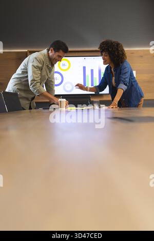 Diverse coworkers reviewing documents on conference table, with monitor showing charts Stock Photo