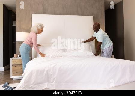 Smoothing duvet senior couple arranging king-size bed in master bedroom, highlighting plush pillows Stock Photo