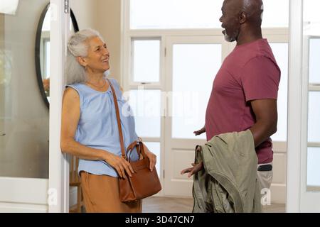 Smiling Senior couple greeting each other in home entryway, with handbag, olive green jacket draped Stock Photo