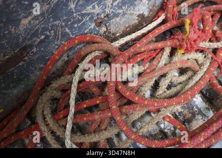 Close up of an old red rope in chaotic tangled mess on dirty surface. This abstract, worn texture provides detailed background with feeling of confusi Stock Photo