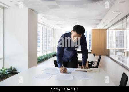 Concentrated young African man study statistic documents on office table Stock Photo