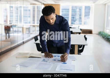 Young Black businessman stand at desk engaged in project research Stock Photo