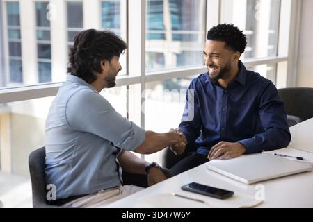 Two happy friendly diverse businessmen shake hands at office desk Stock Photo