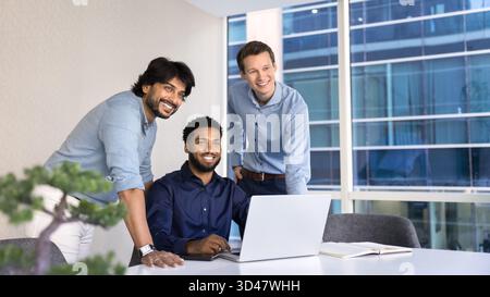 Three diverse male colleagues looking forward distracted from computer work Stock Photo