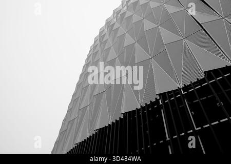 Abstract low-angle view of a perforated metal facade with triangular panels and vertical fins, photographed in Helsinki, Finland, on an overcast day. Stock Photo
