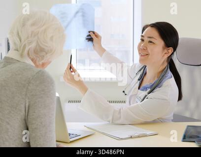 Female physician discussing positive results of MRI examination with female senior patient, showing her radiograph and smiling Stock Photo