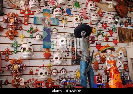 Colorful Day of the Dead masks, crosses, and skeleton figurines fill a vibrant souvenir shop wall, showcasing traditional Mexican folk art Stock Photo