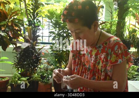 Asain elder woman sewing cloth for repairing in home front yard Stock Photo
