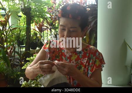 Asain elder woman sewing cloth for repairing in home front yard Stock Photo