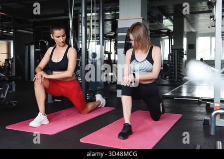 Group of young strong ladies on sportswear stretching legs on yoga mat after workout. Concept of fitness, training and lifestyle. Stock Photo