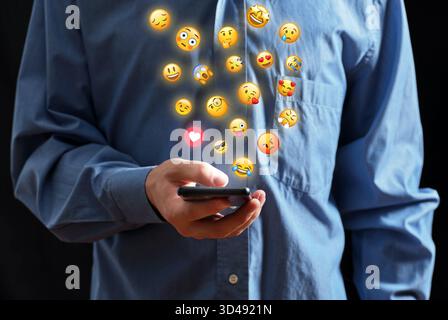 Person holding a mobile phone with various emoji icons floating above, representing digital communication and emotional expression Stock Photo