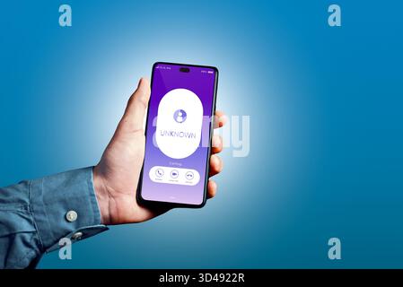 Hand holding a mobile phone displaying an incoming call from an unknown number on a blue background, representing scam risk Stock Photo