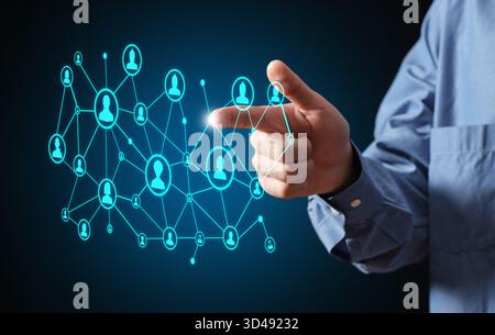 Businessman hand interacting with a glowing digital network of people icons, representing global communication and technology Stock Photo