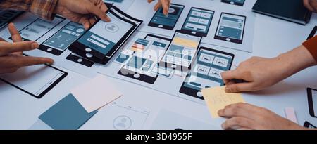 A dynamic workspace showcases hands engaged in a collaborative design process, creating mobile app prototypes and wireframes, reflecting teamwork and Stock Photo