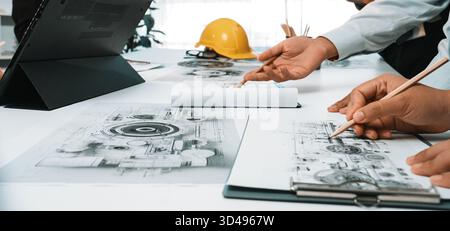 Engaged team discussing technical drawings and project plans in a bright office environment. Essential tools and documents are visible, highlighting Stock Photo