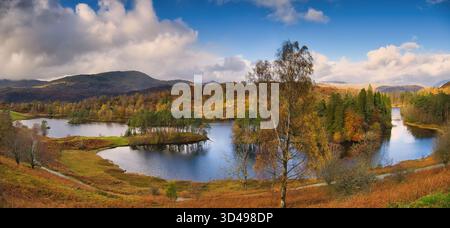 A panoramic shot of Tarn Hows from the viewpoint with the autumn colours of the surrounding woodland deep and rich Stock Photo