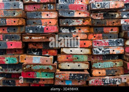 Pile of old, rusted metal pieces with numbers and letters on them. The colors are red, green, and black Stock Photo