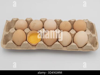 Fresh brown chicken eggs in carton box with one broken egg showing yolk, natural food concept Stock Photo