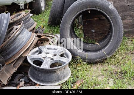 Old vehicle rims and tires near wooden wall. Automotive waste and recycling theme with rusty metal and worn rubber outdoors. Stock Photo
