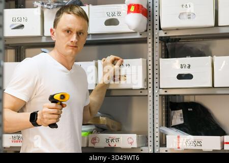 Employee scanning box label in storage rack. Male worker holding scanner to container code on shelf in order pickup warehouse Stock Photo