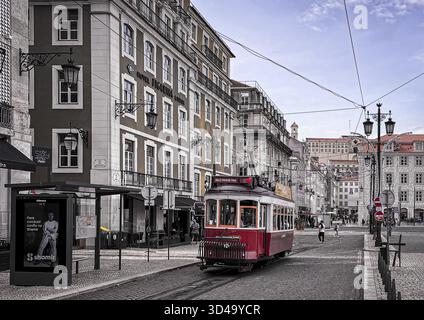 City view of a classic red tram in Lisbon, Portugal. The scene features historic buildings with typical Portuguese architecture, cobblestone streets a Stock Photo