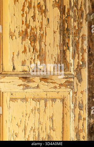 Peeling yellow paint on weathered wooden door creating rustic texture Stock Photo