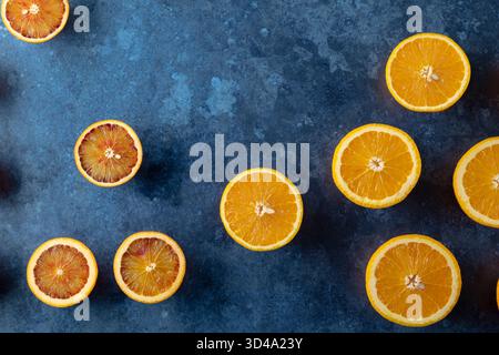 Sliced citrus fruit including oranges and blood oranges on a blue textured surface Stock Photo