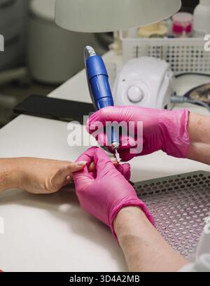 Food, Nail technician using an electric file to shape nails during a professional manicure, wearing pink gloves at a salon table Stock Photo