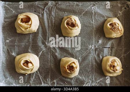 Bake craft rolls with cinnamon and sugar. process of making cinnamon rolls. dough on baking sheet, bun shape Stock Photo