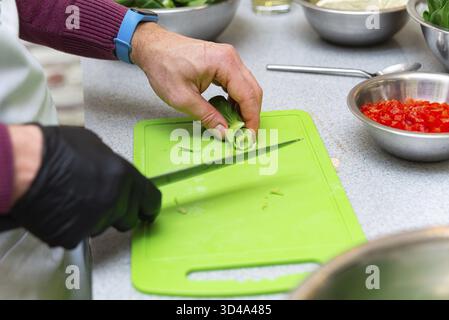 Food, Close-up of hands cutting fresh bok choy on a green cutting board in a kitchen with chopped vegetables nearby Stock Photo