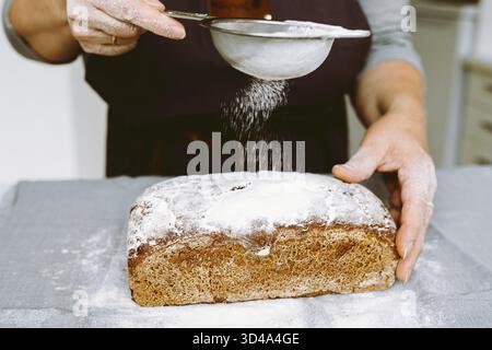 Close-up hands of female chef sprinkles rectangular rye bread with flour for long storage Stock Photo