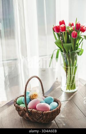 Pastel colored Easter eggs in a basket with tulips in a vase Stock Photo