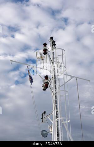 A close view of a white ship mast with navigation lights and rigging set against a cloudy blue sky, conveying nautical technology, safety, and maritim Stock Photo