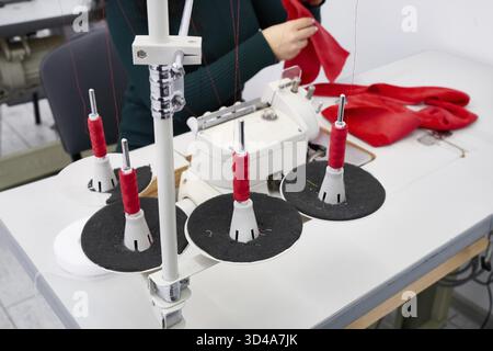 Young woman using professional overlock sewing machine in workshop. Equipment for edging, hemming or seaming clothes at tailors shop Stock Photo