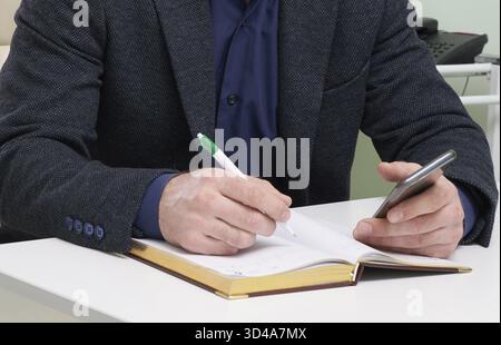 Mature man sitting in his office and writing in notepad Stock Photo
