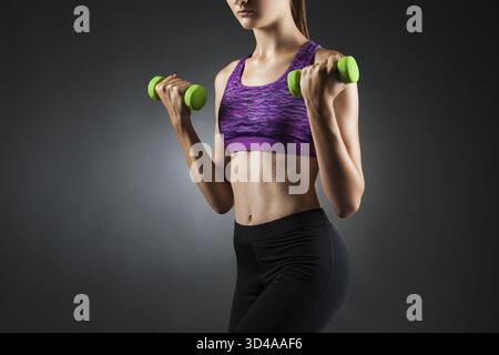 Beautiful woman doing biceps exercises with green dumbbells. Studio portrait black vignette background Stock Photo
