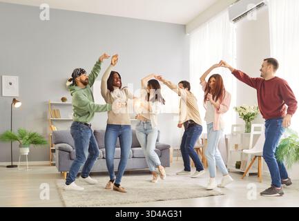 Group of happy diverse friends dancing in pairs to music, having fun together during house party. Stock Photo