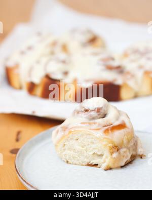 Close-up of a freshly baked cinnamon roll with creamy vanilla icing, served on a ceramic plate. Stock Photo