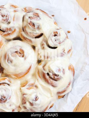 Close-up of a freshly baked cinnamon roll with creamy vanilla icing, served on a ceramic plate. Stock Photo