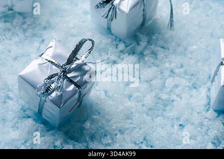 Festive silver Christmas gift box with a shiny ribbon placed on a blue snowy background. Stock Photo