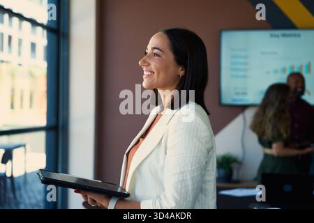 Side view of smiling young businesswoman in smart casual with tablet in boardroom at office Stock Photo
