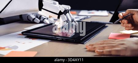 A futuristic robot hand interacts with a digital tablet on a sleek modern workspace, surrounded by colorful sticky notes and design documents Stock Photo